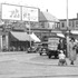 Enlargement.  In this 1938 Jamaica Plain view, car 5338 travels down Centre Street. A tiny Atlantic & Pacific (A&P) grocery store can be seen with a large awning below the billboard. To the right, just to the left of the two women walking with a baby stroller, sits a truck parked at the curb with a sign, "Gentles Swedish Health Bread", afixed to the rear.