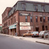 Surret Market on Green St. looking west toward Centre St. Note the fading paint just below the roof line advertising a long-defunct plumbing and heating supply company. This four-story mansard-roofed building was constructed in 1879 by Canadian immigrant Alfred Pappineau. It housed a carriage factory and livery stable. The building seen beyond the old carriage factory is the Hotel McKinley built shortly after 1890 by Patrick Meehan. Built along with a sister building, the Hotel Morse, these building were actually apartment buildings with retail space on the first floor and apartments on the floors above.