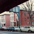 This view looks down Washington St. with the old Orange Line T structure overhead. The low blue building on the left is the Brookside Health Center. A portion of the Evangelical Church on the corner of Washington and Cornwall Streets is visible on the right. The two triple-deckers are between Ackley Place and Cornwall Street.